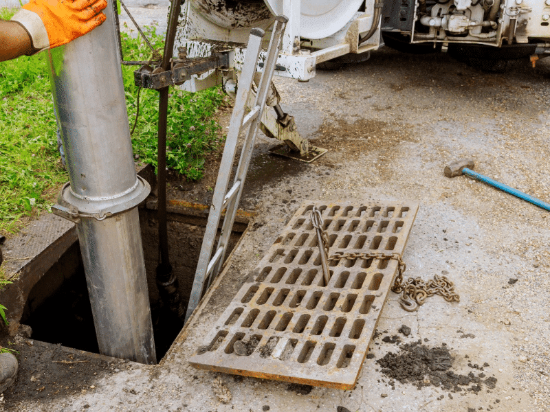 Worker cleaning sewer drain with equipment.