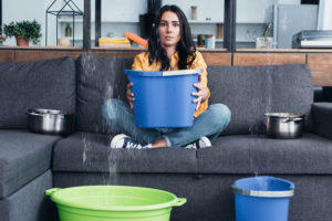 Woman catching leak water with bucket indoors.